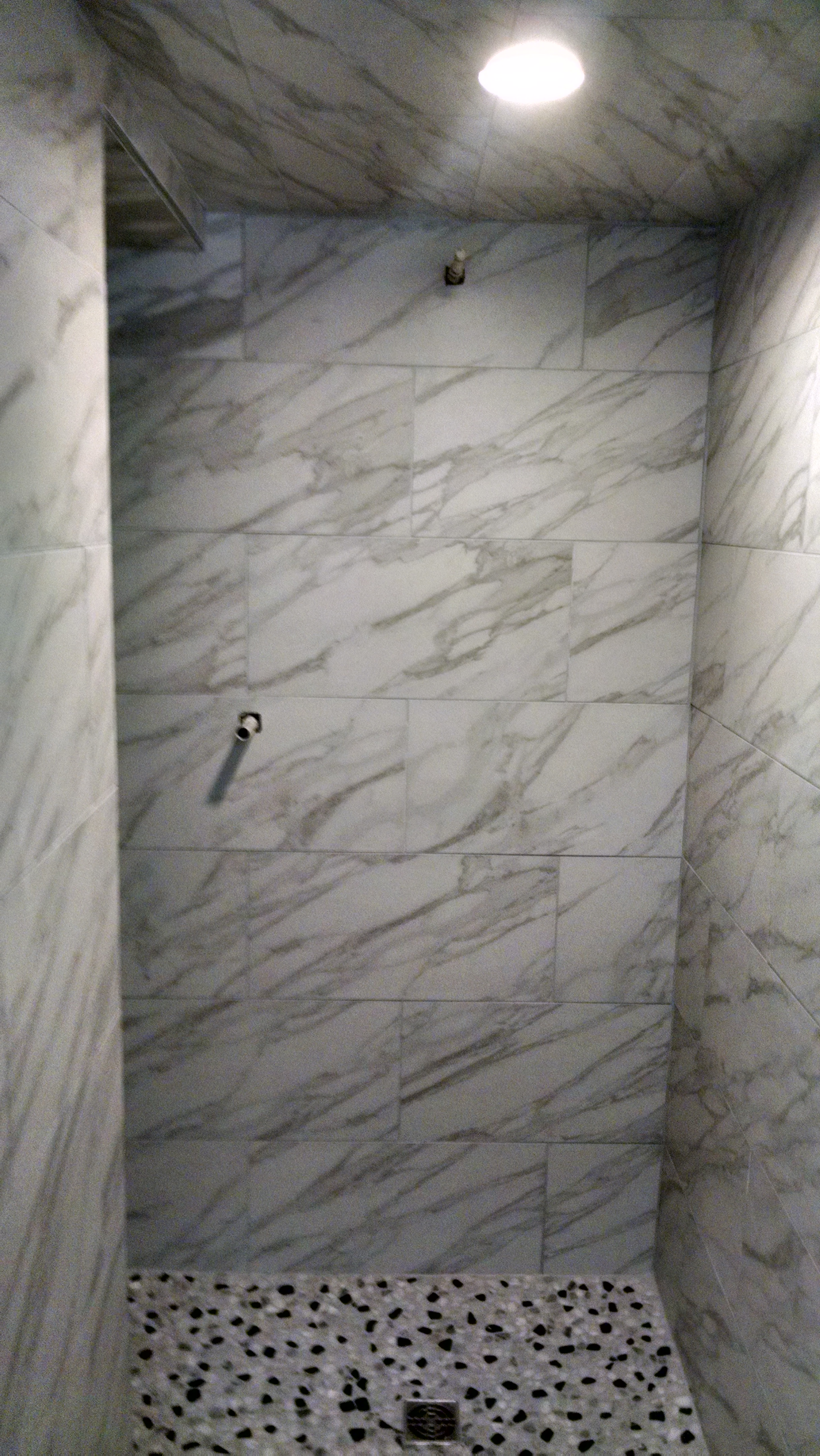 Shower tiled with marble look tile and small rock floor